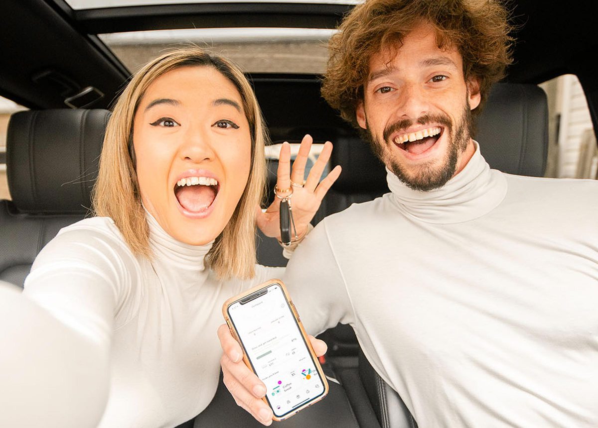 A couple smiling in a car while holding a smart phone